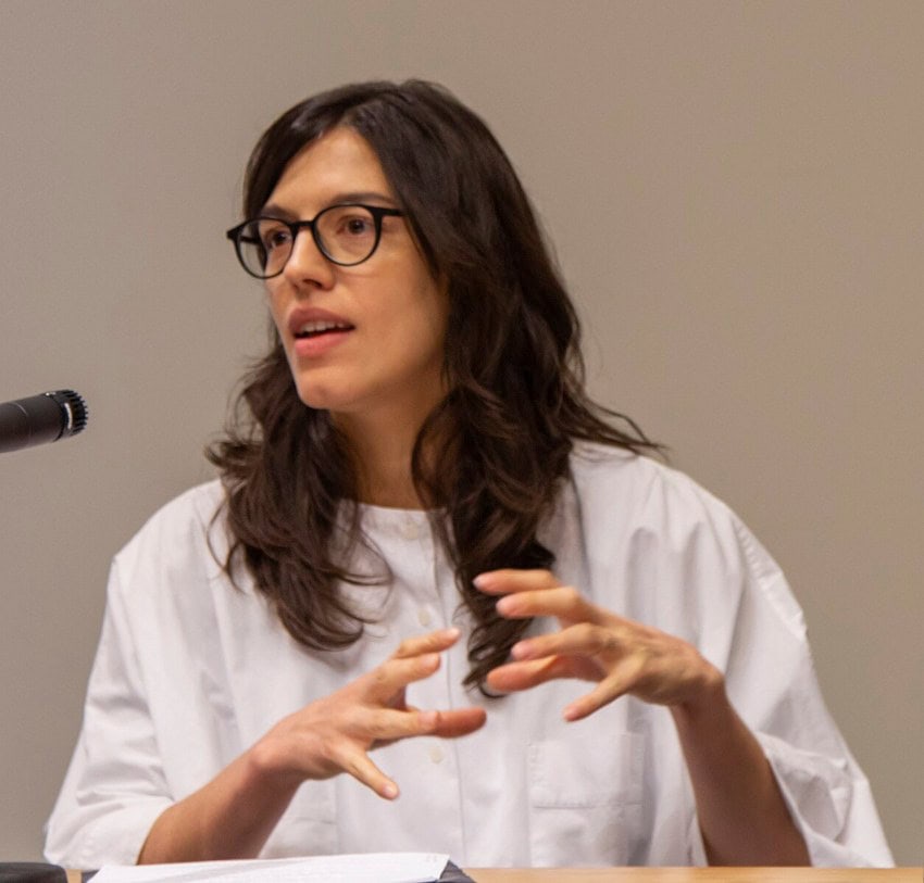 Mexican architect Gabriela Etchegaray speaking at an event. She's sitting at a table with a microphone nearby.