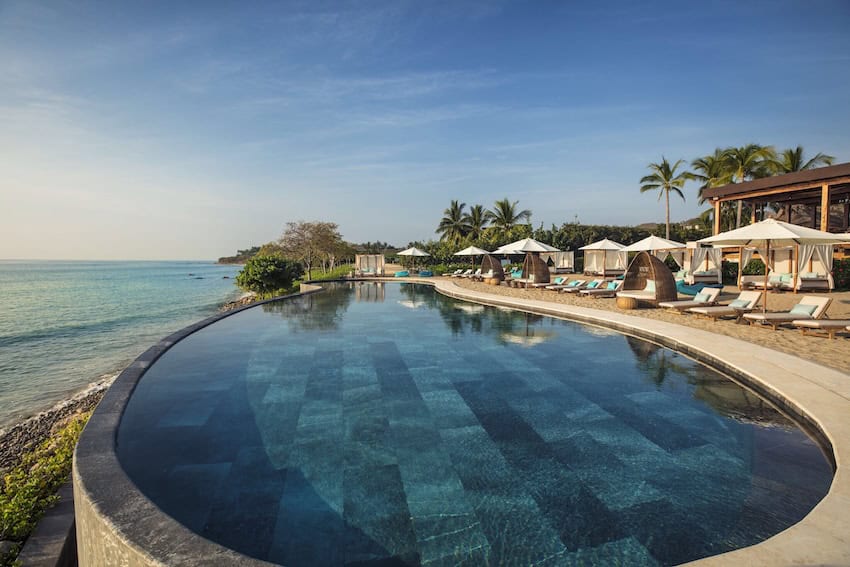 Infinity pool by the ocean at Club Sufi in Punta Mita, surrounded on one side by elegant deck chairs and outdoor day beds.